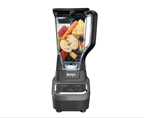 Ninja blender with fruits and vegetables in the pitcher on a dark base with control buttons