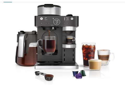 Black dual-brew coffee maker with a carafe, surrounded by various coffee beverages in cups and brewing pods