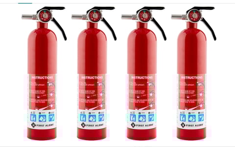 Four red fire extinguishers with black handles and white instruction labels arranged in a row