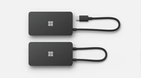 Two black Microsoft portable SSDs with attached USB cables arranged vertically against a light background